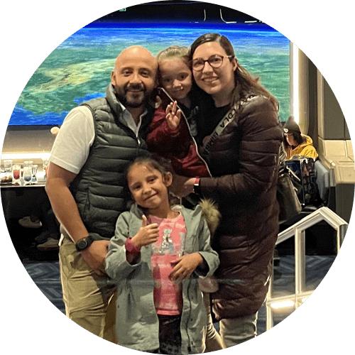 An adult woman, adult man, and two young girls pose together in the Space 220 Restaurant at the Walt Disney World Resort. The restaurant windows simulate a panoramic view of Earth from outer space.