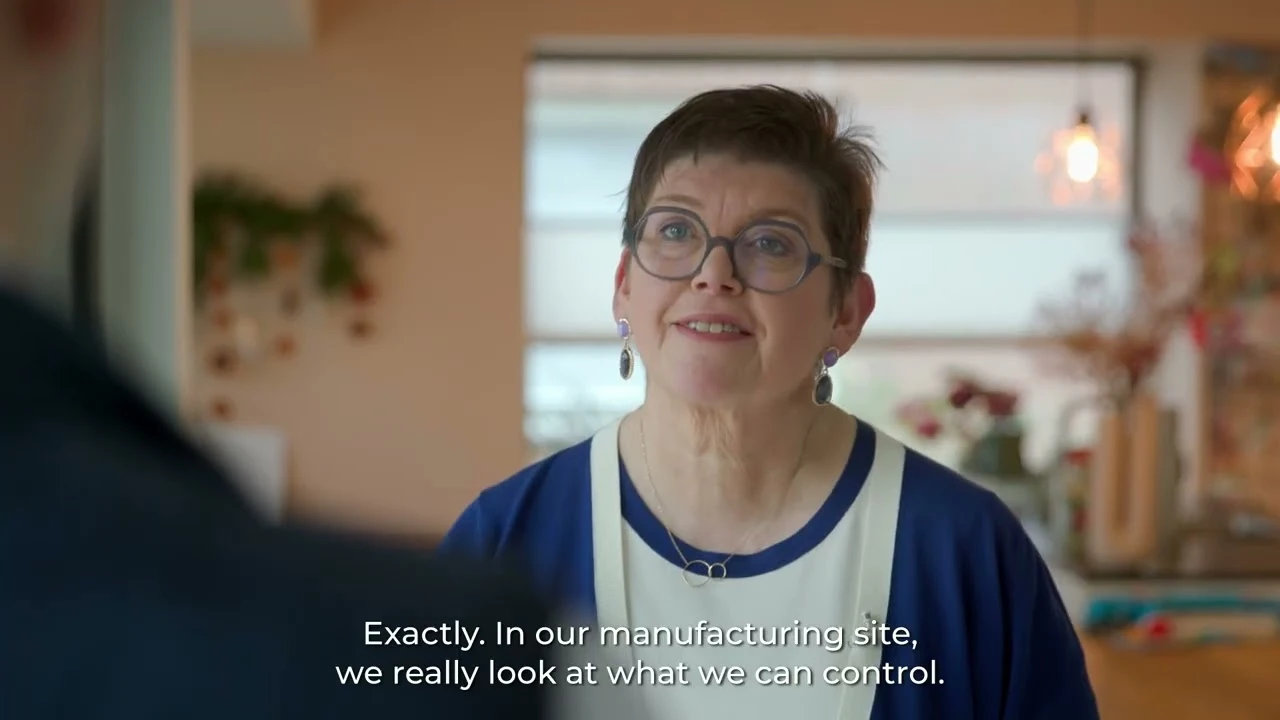 Person wearing glasses speaking indoors, with kitchen background.