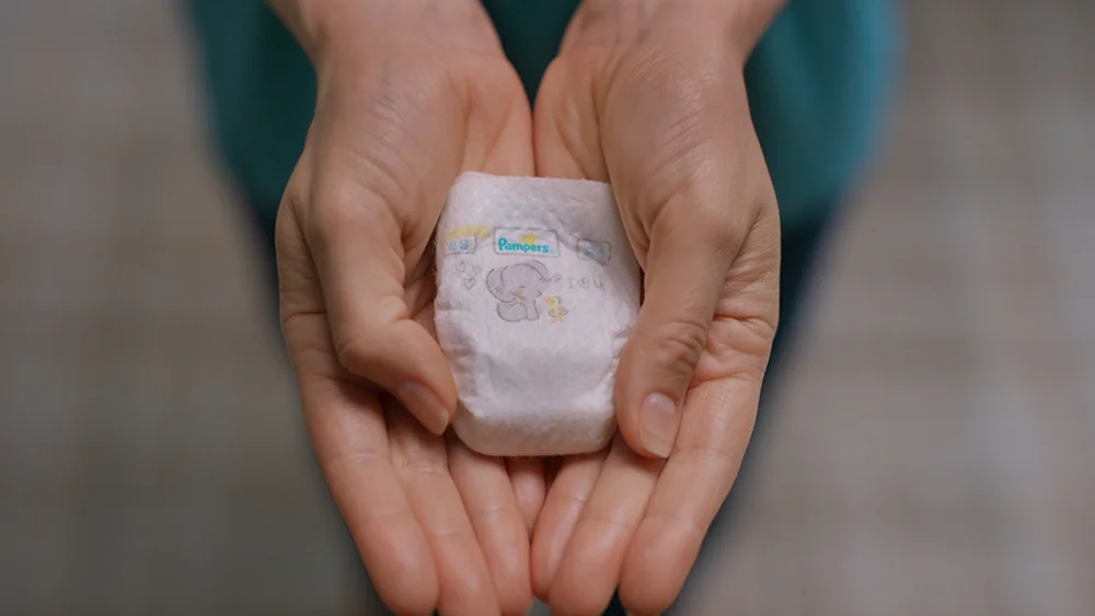 Cupped hands holding the Pampers Swaddlers Pxxs diaper.
