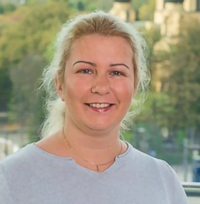 A woman with blonde hair, in a grey shirt, smiles.