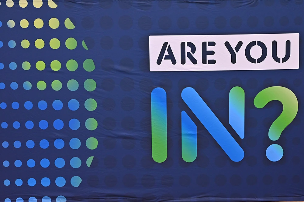 A navy blue banner with blue and green dots on the left and text that says “Are you IN?” on the right.