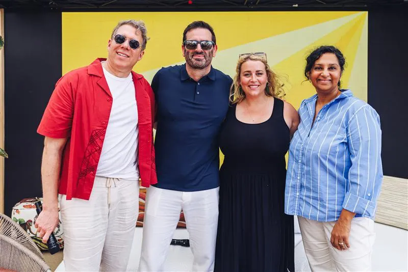 Two women and two men wearing sunglasses stand together smiling on stage.