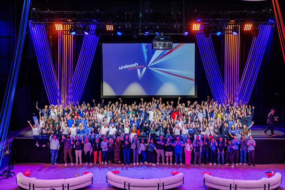 A large group of men and women gathered together on and in front of a large stage.