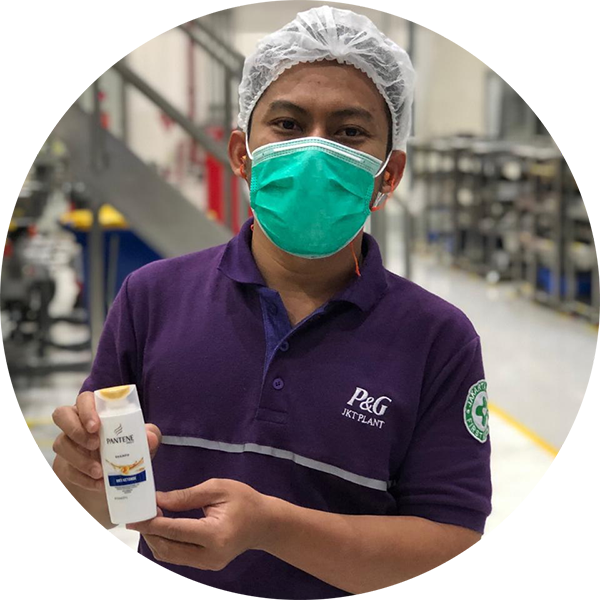 A man wearing a protective mask, holding a bottle of Pantene shampoo