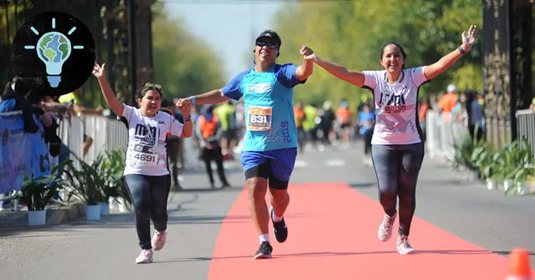 A young Hispanic girl, Hispanic man and Hispanic woman hold hands as they run across a marathon finish line.
