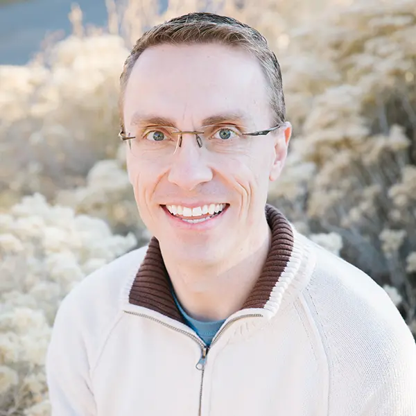 A man with short brown hair and glasses smiles.