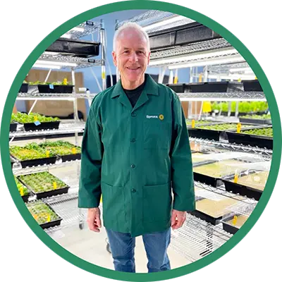 A man in a green lab coat in a plant cultivation facility.