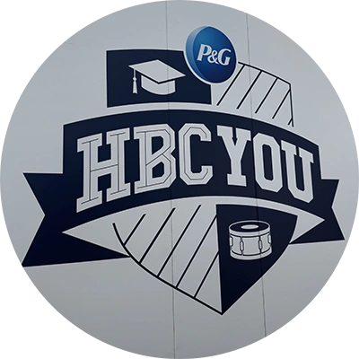 A logo of a shield with illustrations of a graduation cap and a drum. White letters say “HBC You”.
