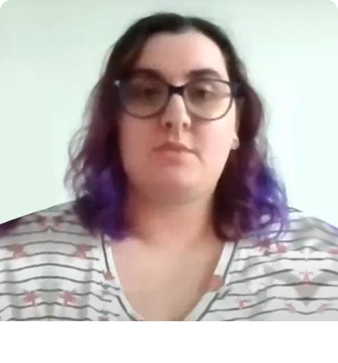 Woman looking towards the camera. She is wearing glasses and has long wavy hair.