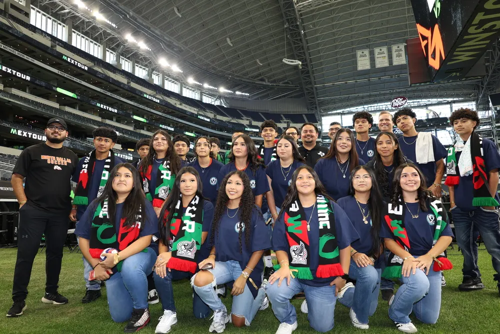 A group of young people in navy blue t-shirts and jeans pose for a photo on a soccer field.