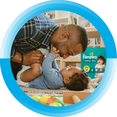 A father is looking at his baby. A package of Pampers Baby-Dry diapers is in the background. 
