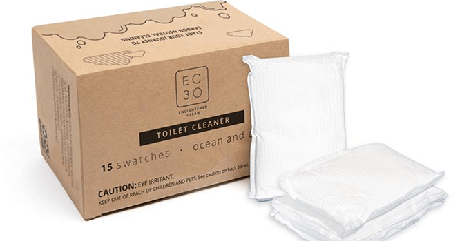 A brown cardboard box features the blue EC30 typeface logo and text with product details for the brand's new toilet cleaner swatches. Three white, rectangular swatches lean against the box.