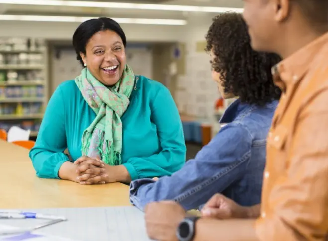 Smiling woman speaks with two colleagues whose backs are to the camera.