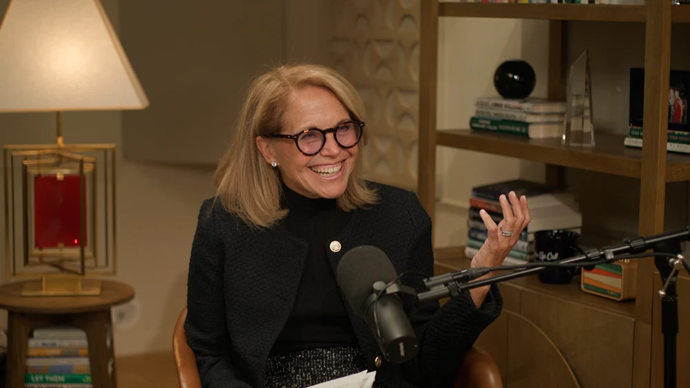 Katie Couric smiling in a room with a microphone