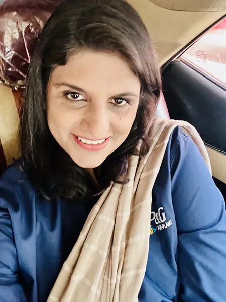 A woman with dark shoulder-length hair, a blue shirt and light brown scarf smiles.