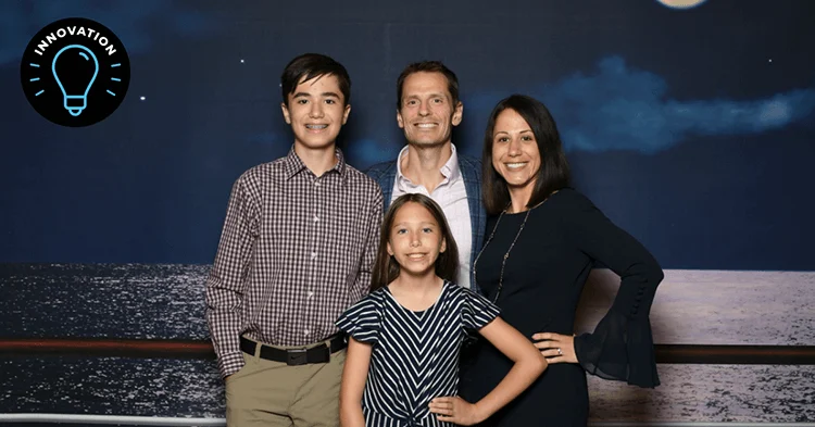 P&G employee Cecilia Colburn, her husband, son and daughter all smile at the camera with a dark backdrop behind them.