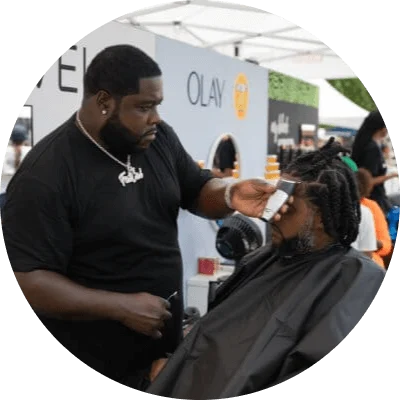 Black consumers experience innovative brands at My Black Is Beautiful, Olay and Bevel stations during the HBCYOU Tour. In the inset, a Black man is seated in a chair and receives a haircut from a barber.