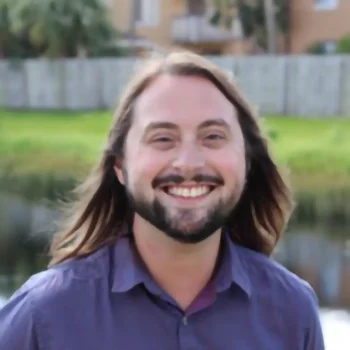 A man with long brown hair, beard and blue button up shirt.