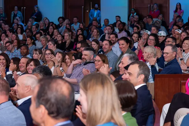 A large group of men and women sit in an auditorium for a large office event.