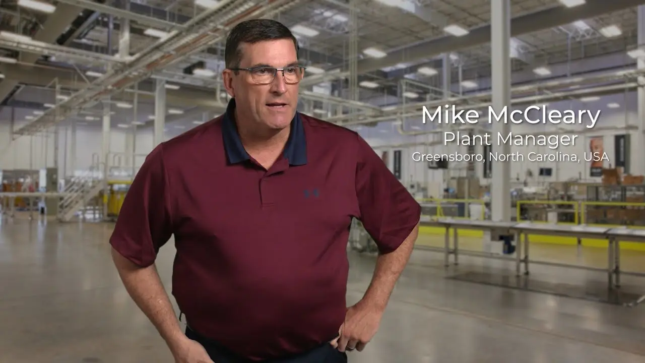 Plant manager standing on production floor with conveyor systems and industrial equipment