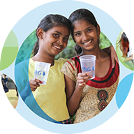 Two smiling girls standing next to each other hold clear cups with the "P&G" logo on them. The background includes overlapping light blue and green circles, creating a layered effect. A blue circle outline surrounds the icon.