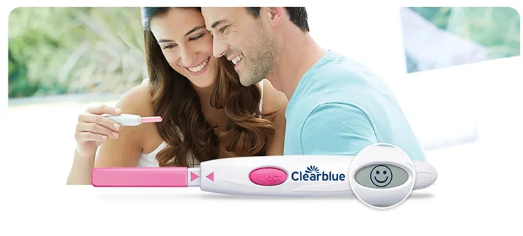A smiling couple holds Clearblue ovulation tests, one displaying a smiling face indicating ovulation. They are excited and hopeful about the positive result.