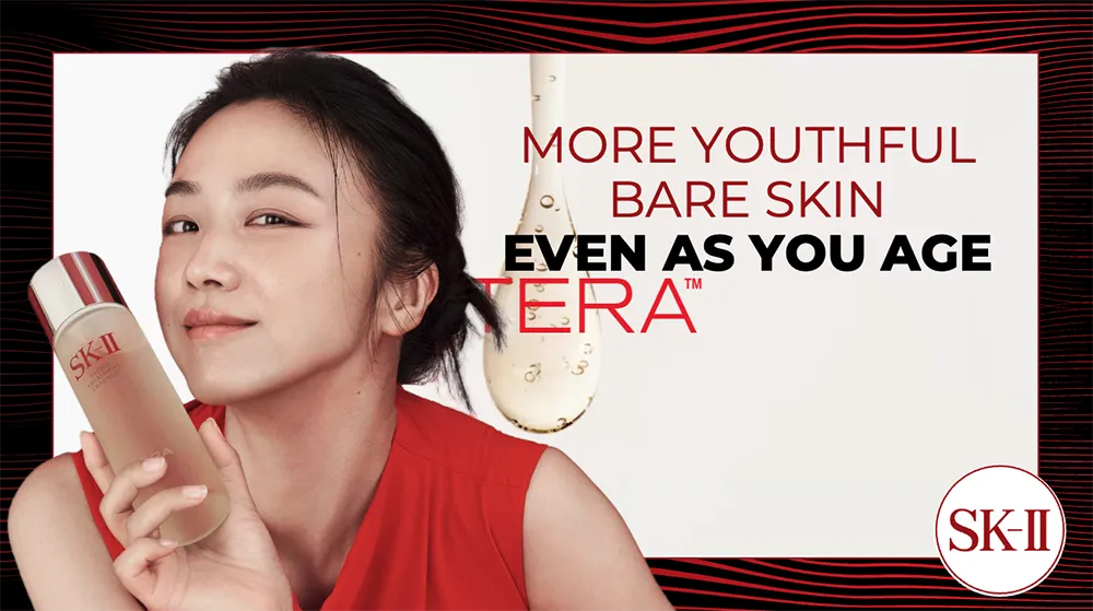 A woman with clear, radiant skin smiles while holding a bottle of facial treatment essence, promoting "More youthful bare skin even as you age."