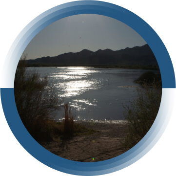 A body of water surrounded by trees. The sun is shining on the water.