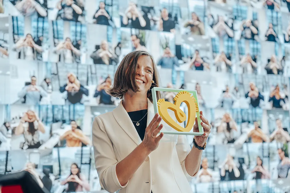 A woman smiles as she stands on a stage and holds up a Pampers logo.