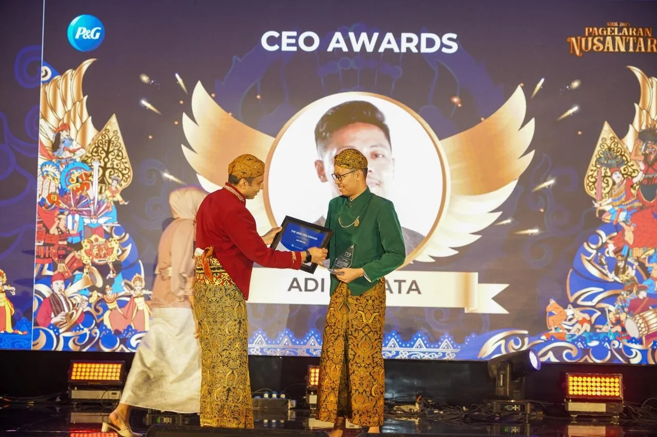 A P&G CEO Awards event. A man hands a framed award to another man. Both are wearing batik sarongs.