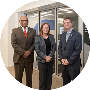 Woman and two men in suits standing together, smiling and looking at the camera