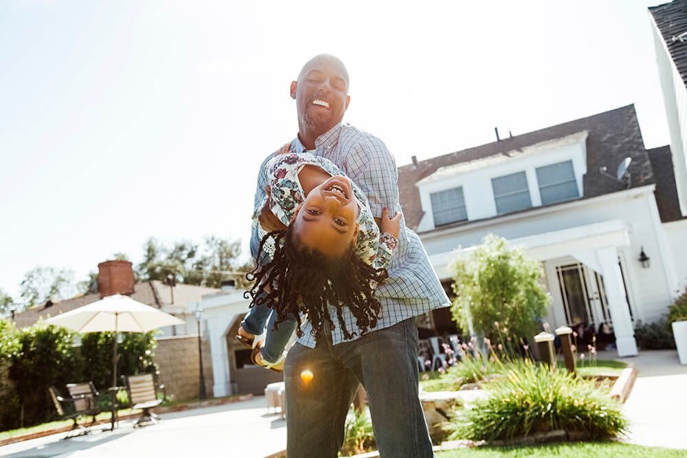 Image of father playfully holding his daughter outside their house.