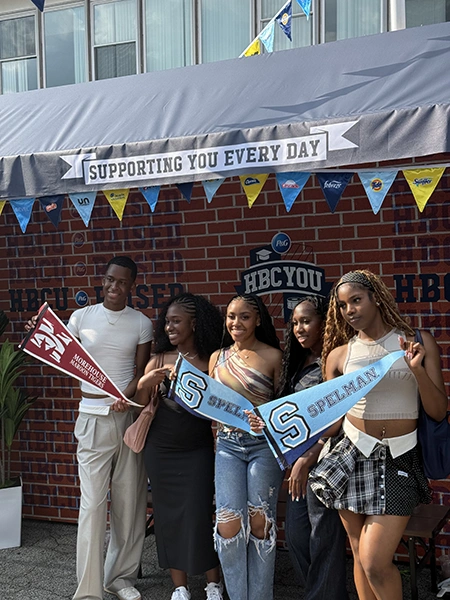 A group of students stand outside holding college pennants.