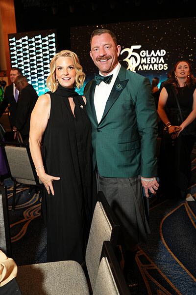Brent Miller stands in a green tuxedo jacket beside GLAAD President and CEO Kate Ellis, who wears a black evening gown. Behind them, the words 35 GLAAD Media Awards are displayed onstage.