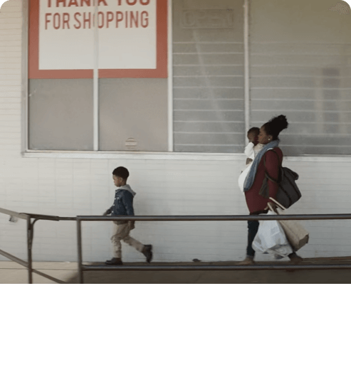 Screenshot from Widen the Screen movie. Woman walking and holding her child in her arms. Her second child walking in front of her.