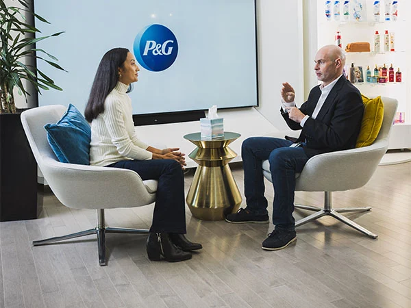 A man and woman sit across from each other in white chairs. The main is communicating with sign language.