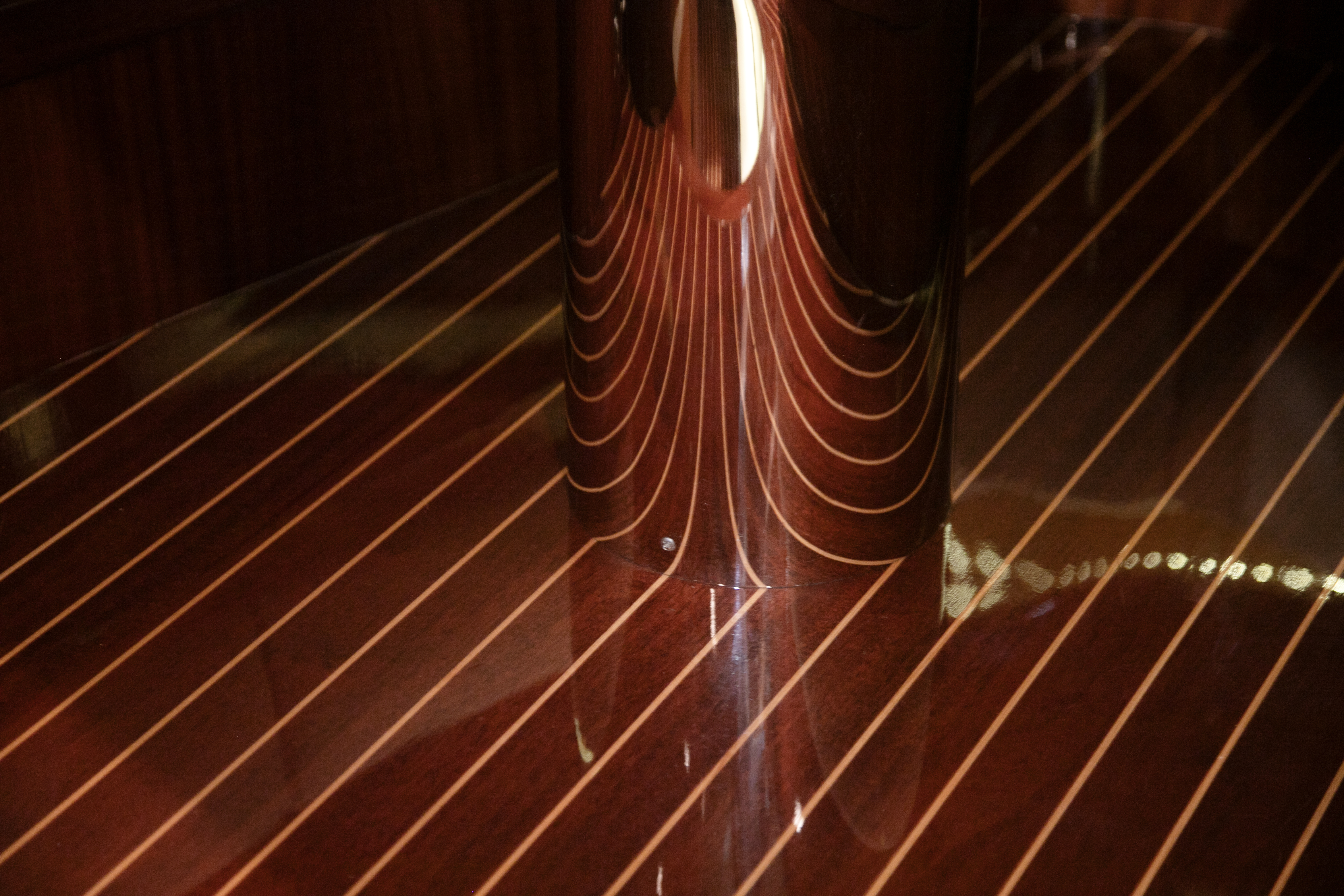 Hand-laid mahogany underfoot, its caulk lines mirrored in the polished steel table foot.