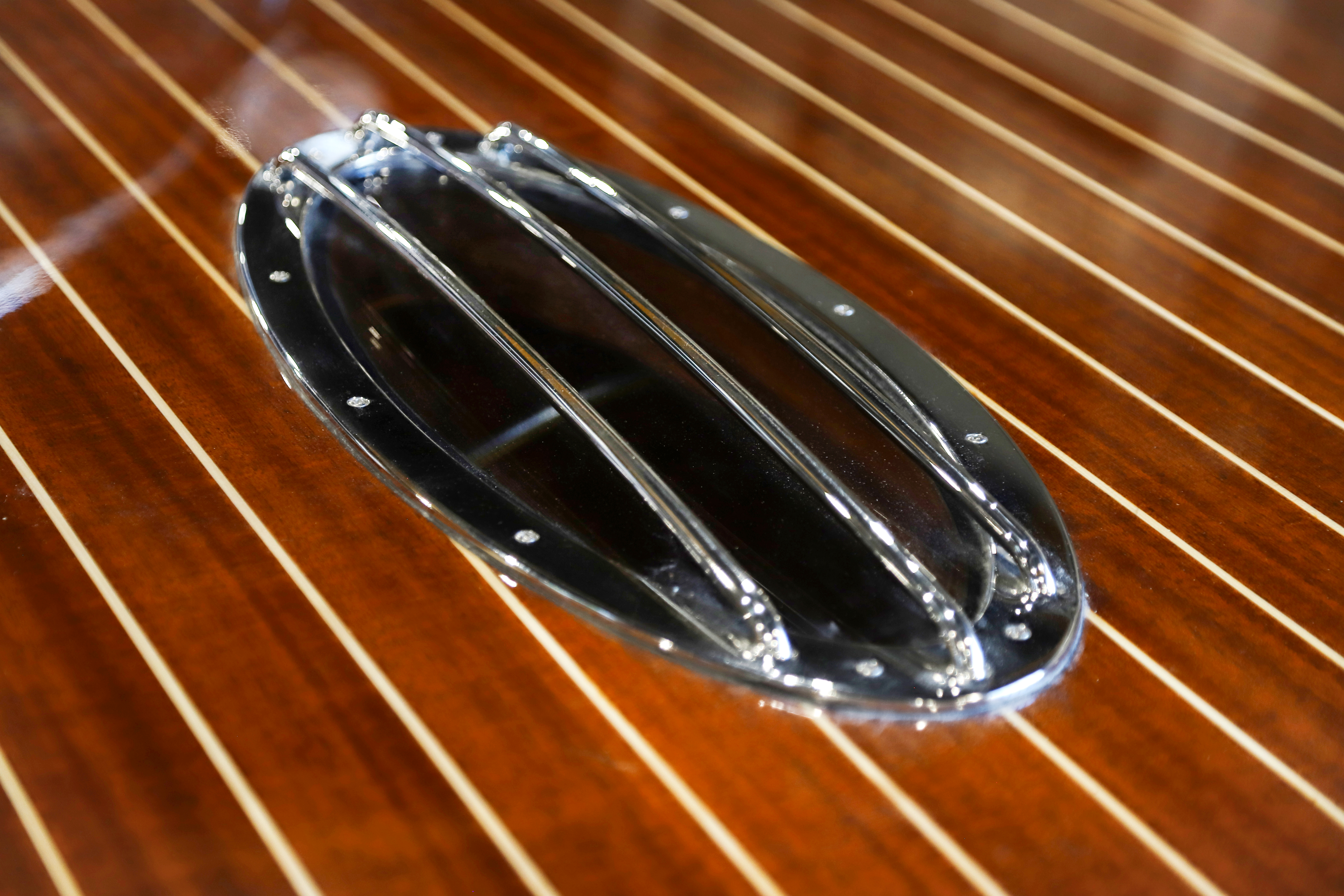 A chrome-rimmed deck window, flush in the mahogany, lighting the cabin below.
