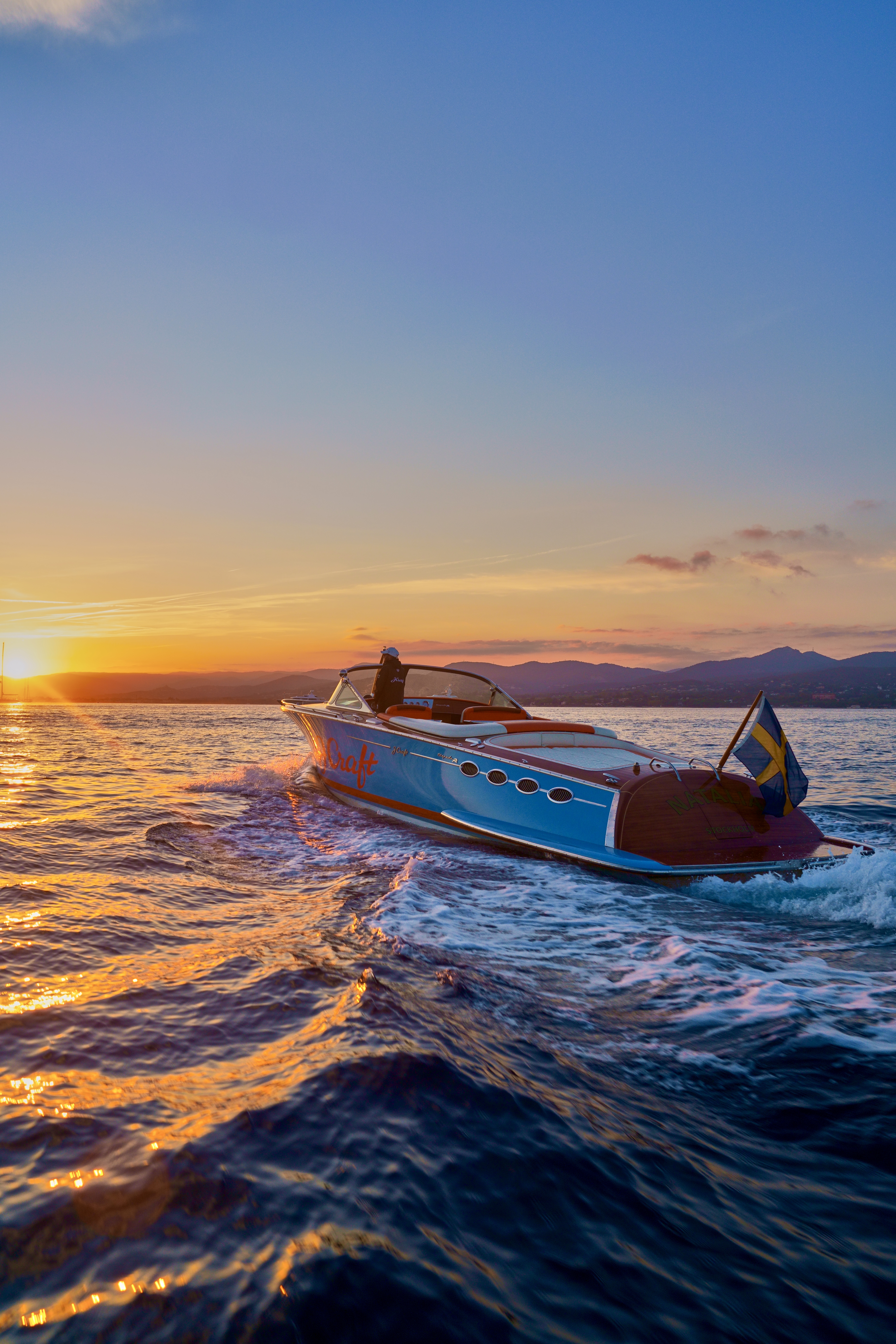J Craft Torpedo luxury runabout with light-blue hull and mahogany transom cruising at golden hour on calm water