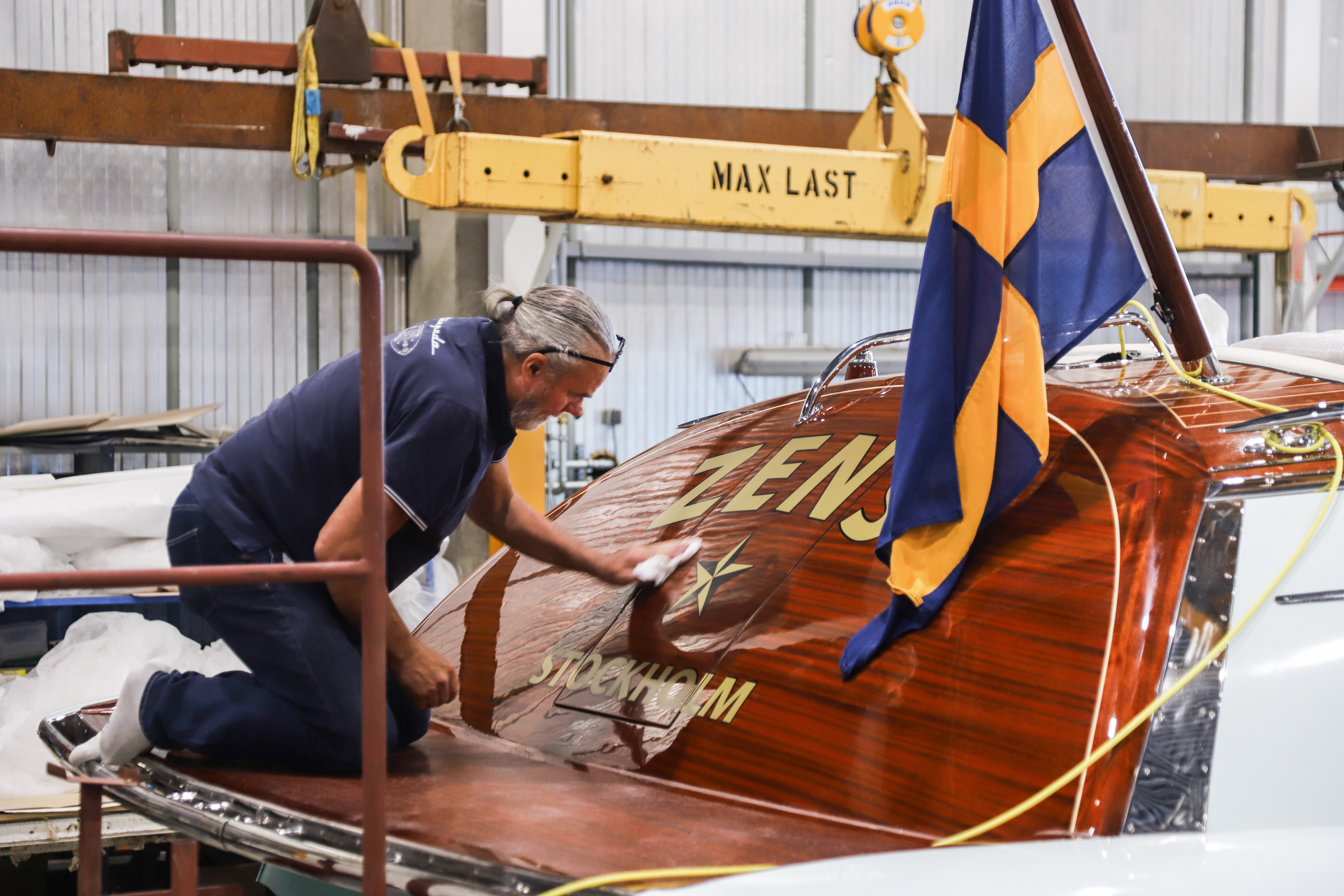 Hand-polishing the mahogany transom, beneath the Swedish flag.