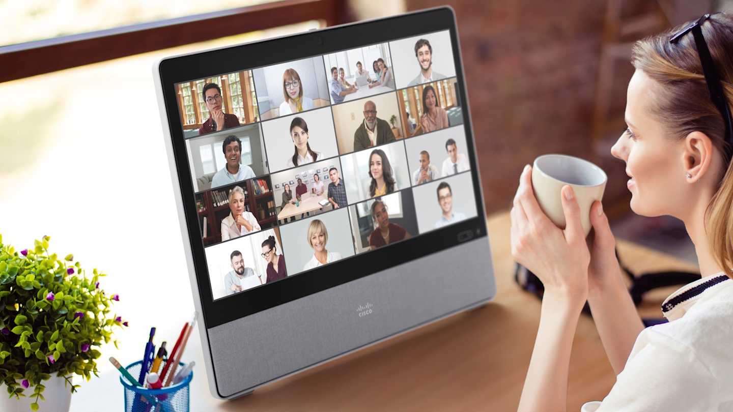 Cisco Webex Desk - Woman drinking from cup in front of Desk device with colleagues on screen.