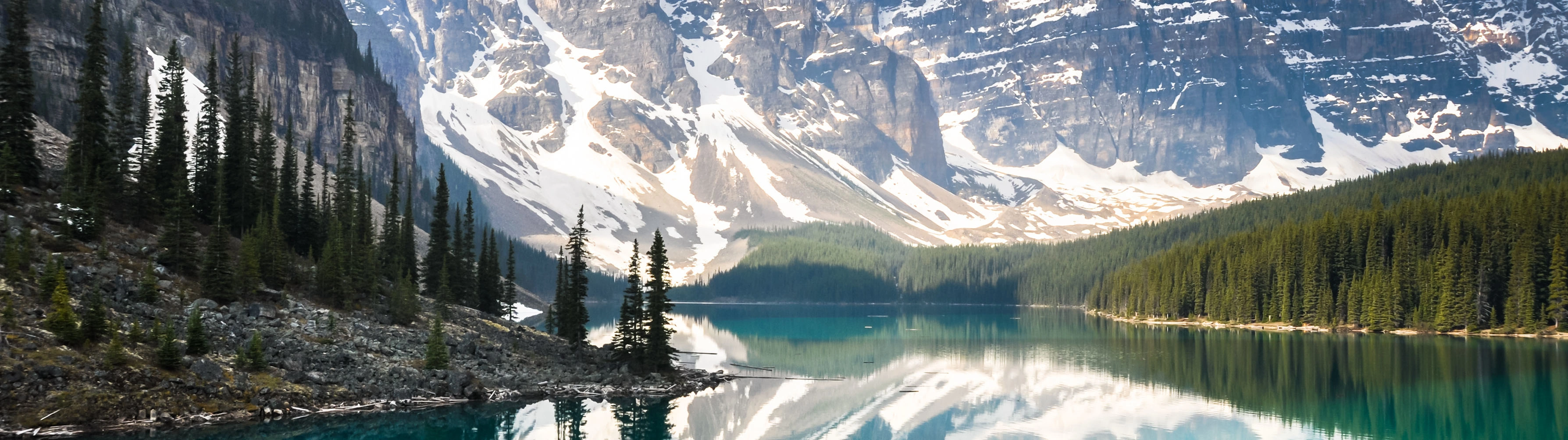 The reflective waters of Lake Louise lie before snow-packed mountain peaks.