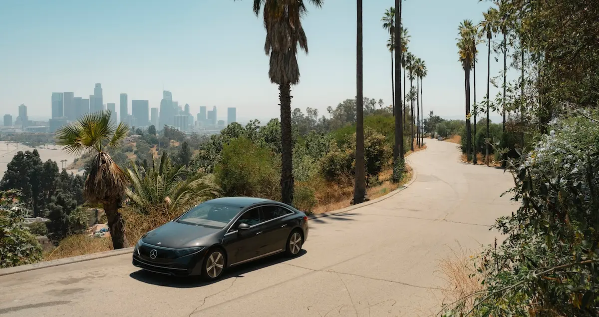 A Blacklane chauffeured Mercedes EQE drives down a road lined with palm trees with downtown Los Angeles in the background.