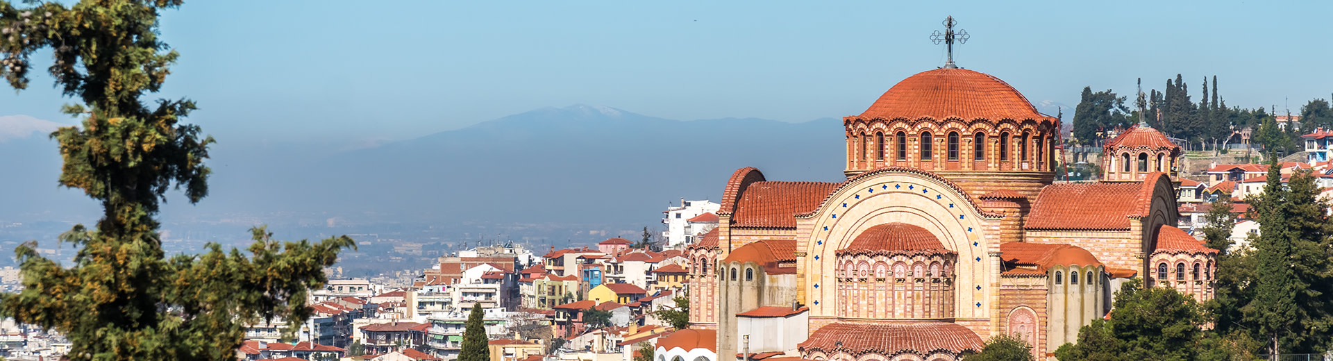 A pale blue sky covers imposing mountains in the background and the ancient city of Thessaloniki in the foreground.