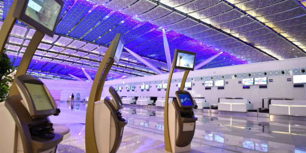 The modern terminal at Jeddah Airport with self-service check-in kiosks and a futuristic ceiling design.