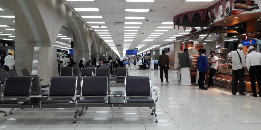 Inside the old terminal of Jeddah Airport, showing seating areas, food stalls, and travelers lining up.