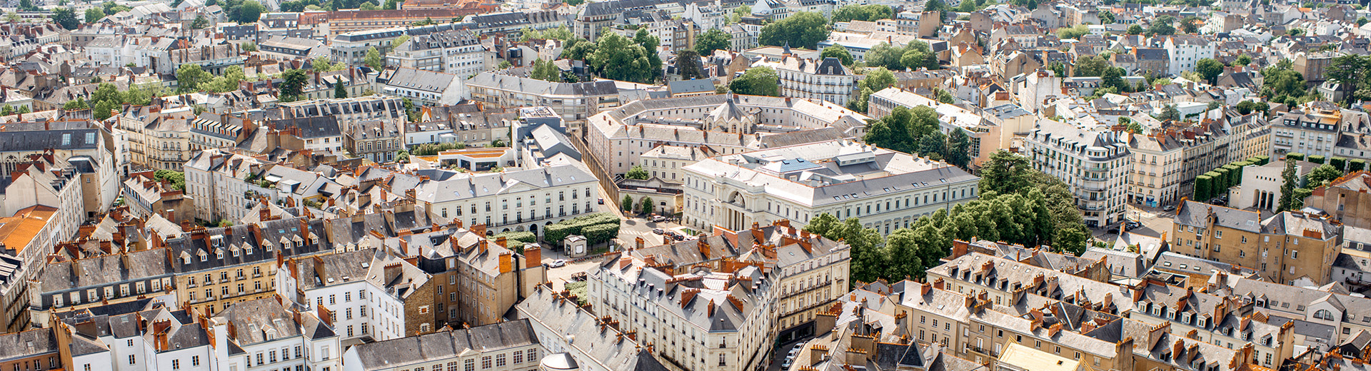 A bright, daytime picture looking down on streets and buildings in Nantes. Green trees nestle among nineteenth-century buildings.