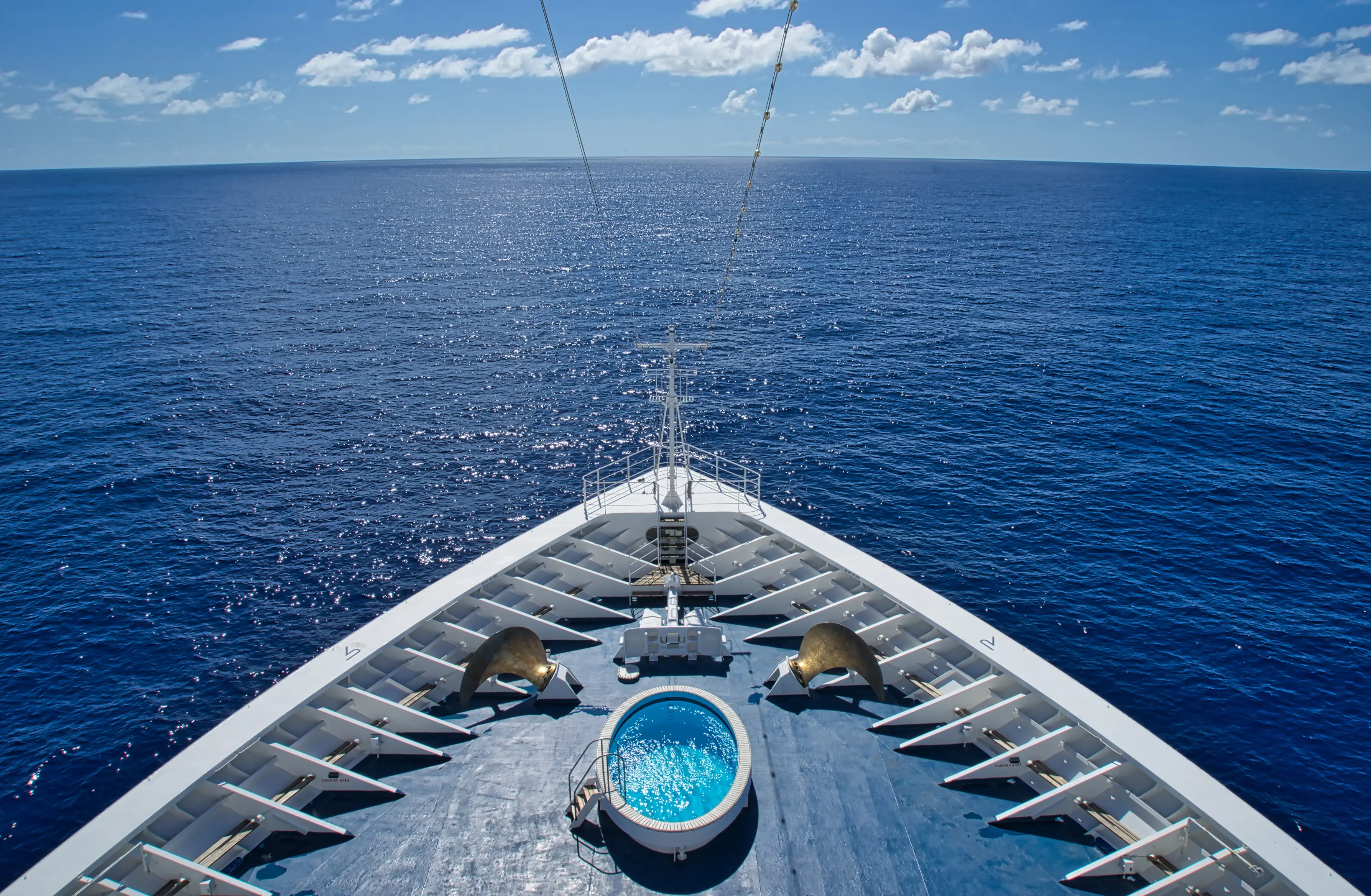 The bow of a luxury cruise liner shot from above with a jacuzzi and the Indian Ocean in the background.