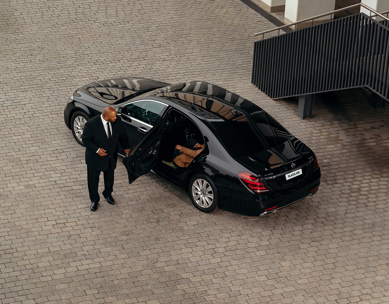 A well-dressed chauffeur opens the door of his stylish vehicle.