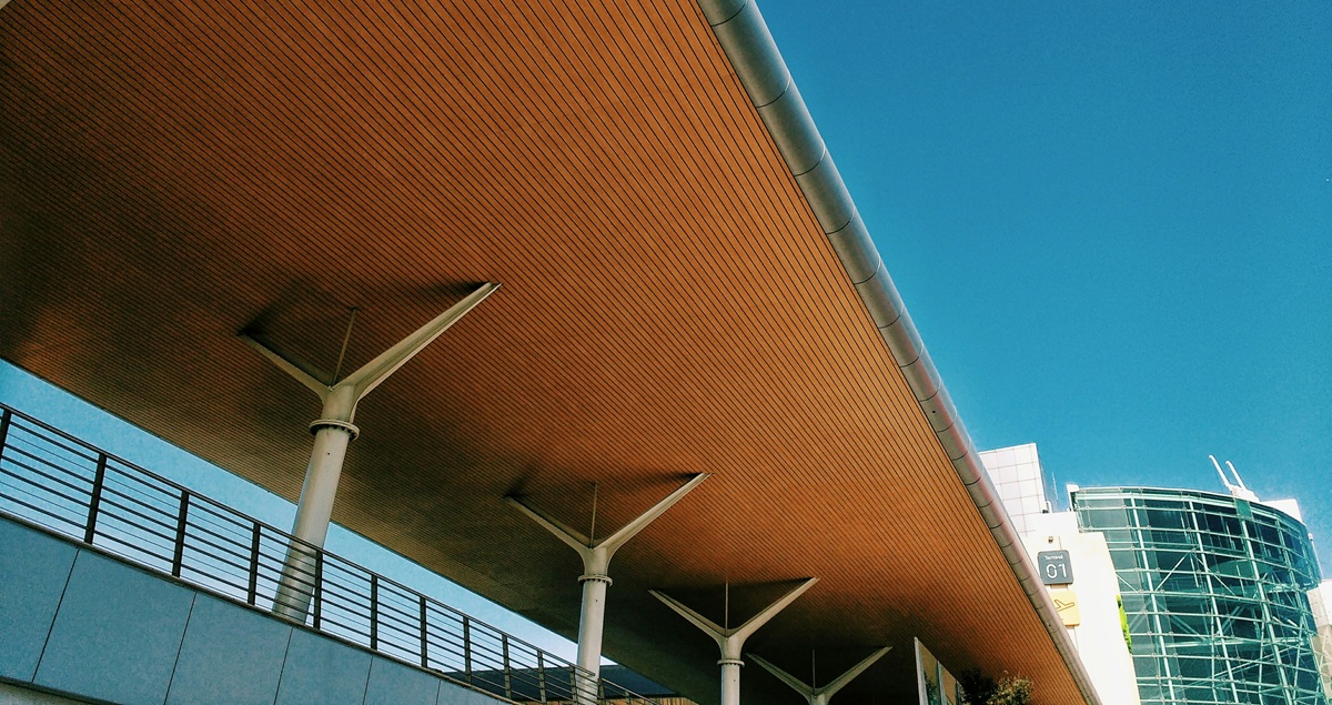 Shot of an exterior walkway outside Lisbon Airport, with the Terminal 1 building in the background and a blue sky above.